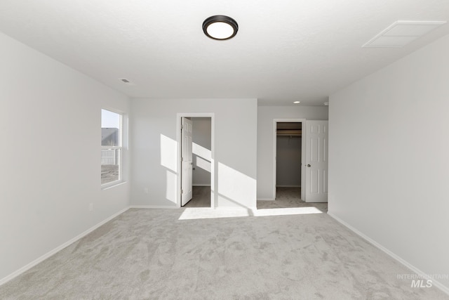 unfurnished bedroom with a walk in closet, light colored carpet, and a closet