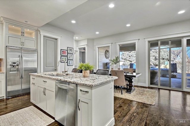 kitchen featuring a center island with sink, sink, light stone countertops, stainless steel appliances, and white cabinets