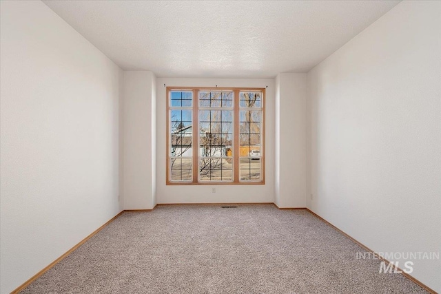 spare room with light carpet, a textured ceiling, and baseboards