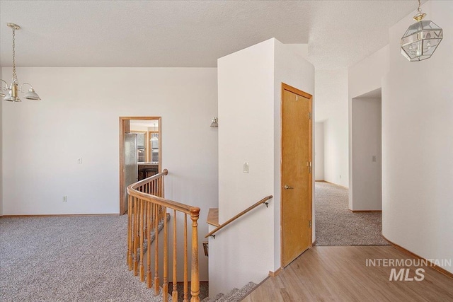 hallway with a chandelier, a textured ceiling, an upstairs landing, and wood finished floors