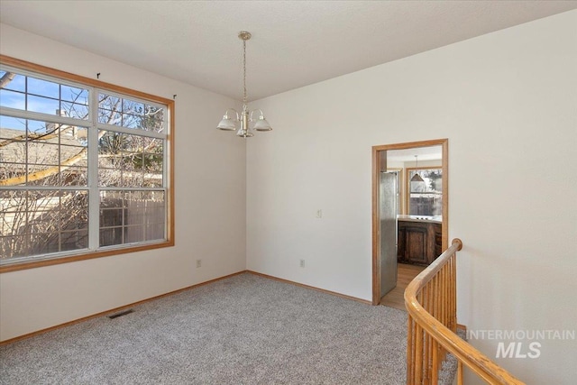 spare room with an inviting chandelier, visible vents, baseboards, and light colored carpet