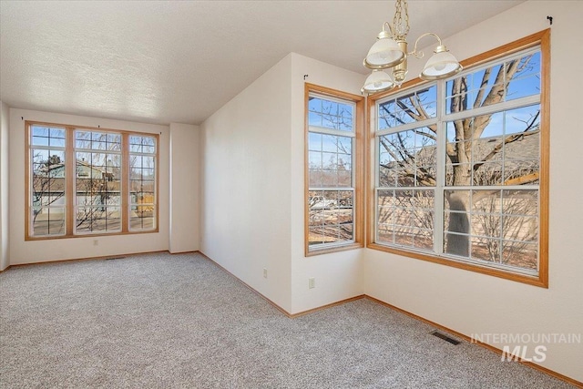 carpeted spare room featuring a textured ceiling, baseboards, visible vents, and a notable chandelier