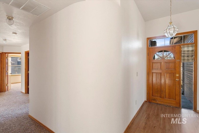 carpeted foyer featuring a textured ceiling, wood finished floors, visible vents, and baseboards