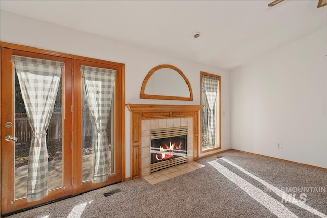 unfurnished living room featuring carpet floors, a tile fireplace, visible vents, and baseboards