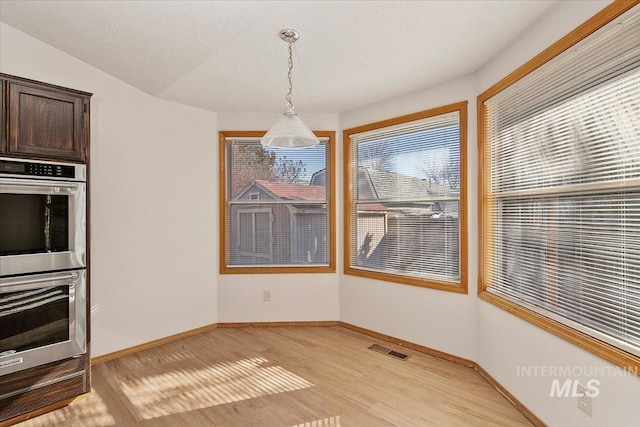 dining room featuring light wood-style floors, visible vents, a textured ceiling, and baseboards