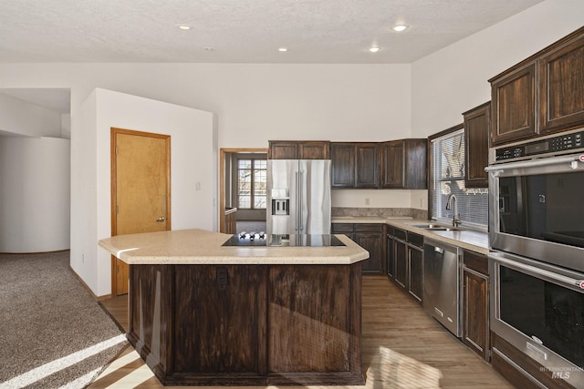 kitchen featuring light countertops, appliances with stainless steel finishes, a sink, dark brown cabinetry, and a kitchen island