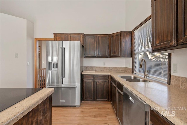 kitchen with stainless steel appliances, light countertops, light wood-style floors, a sink, and dark brown cabinetry