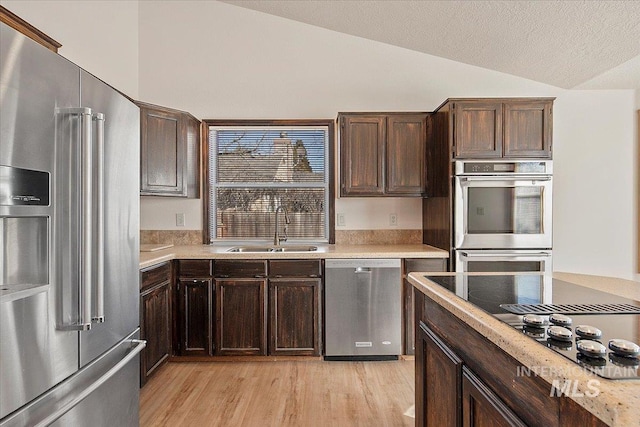 kitchen with vaulted ceiling, stainless steel appliances, a sink, and light countertops