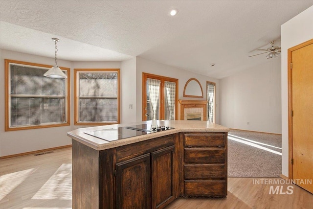 kitchen with light wood-style flooring, open floor plan, decorative light fixtures, light countertops, and a fireplace