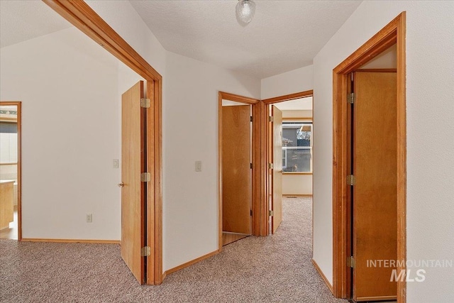 corridor featuring a textured ceiling, carpet, and baseboards