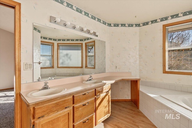 bathroom with wood finished floors, a sink, a bath, and wallpapered walls