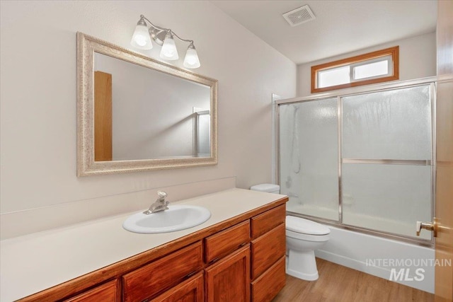 full bathroom with visible vents, bath / shower combo with glass door, toilet, wood finished floors, and vanity