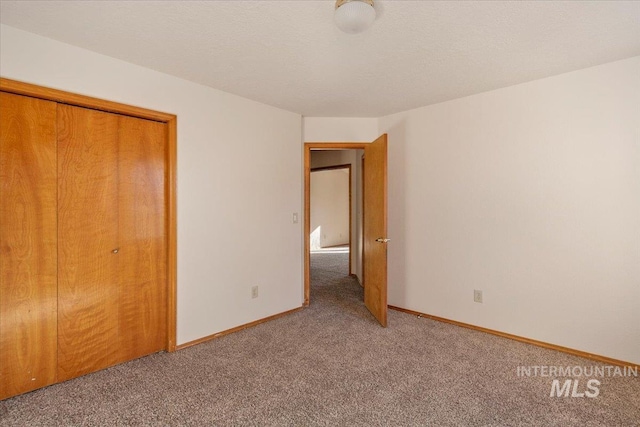 unfurnished bedroom with light carpet, a closet, baseboards, and a textured ceiling