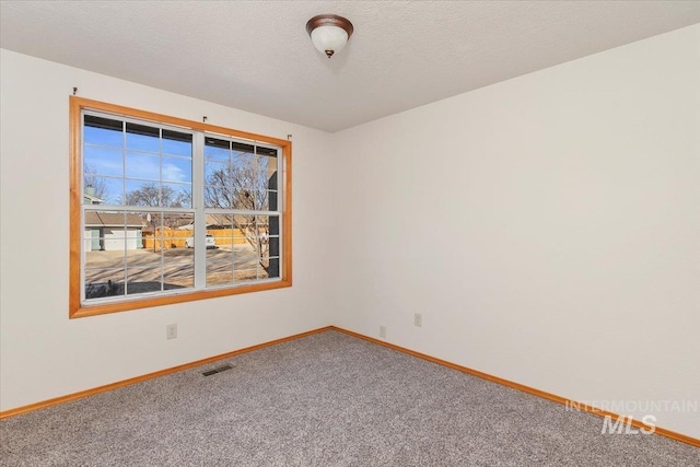 empty room with carpet floors, visible vents, baseboards, and a textured ceiling