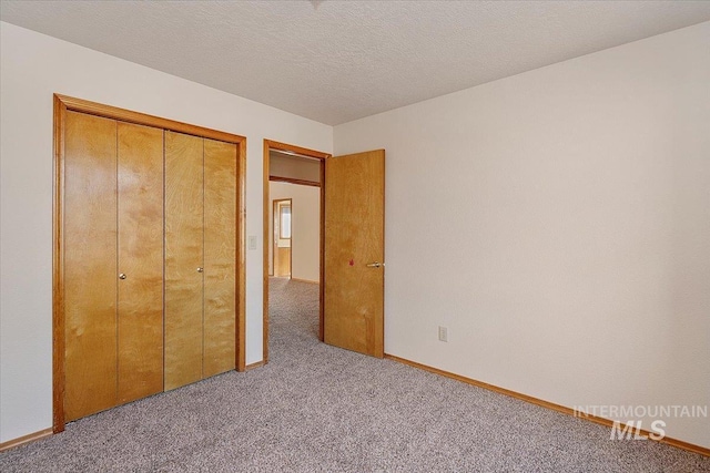 unfurnished bedroom with carpet floors, a closet, a textured ceiling, and baseboards