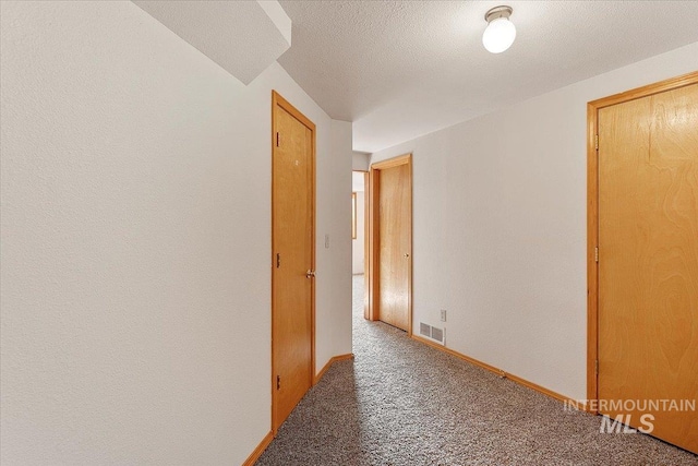 corridor with carpet floors, baseboards, visible vents, and a textured ceiling