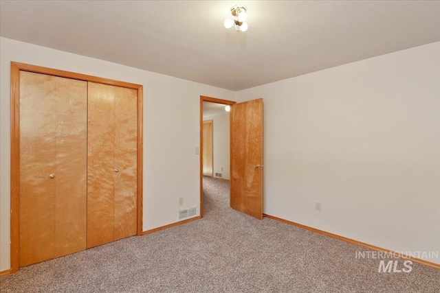 unfurnished bedroom with baseboards, visible vents, a textured ceiling, carpet floors, and a closet