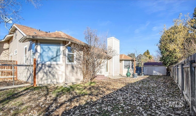 exterior space featuring a fenced backyard, an outdoor structure, a chimney, and a shed