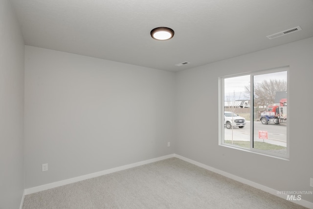 unfurnished room with carpet, visible vents, and baseboards