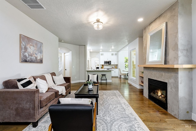 2383 E Lenox Ct, Eagle, ID 83616 - living room featuring arched walkways, wood finished floors, a warm lit fireplace, a textured ceiling, and baseboards