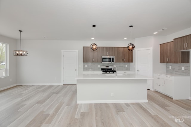 kitchen with stainless steel appliances, hanging light fixtures, backsplash, and light hardwood / wood-style flooring