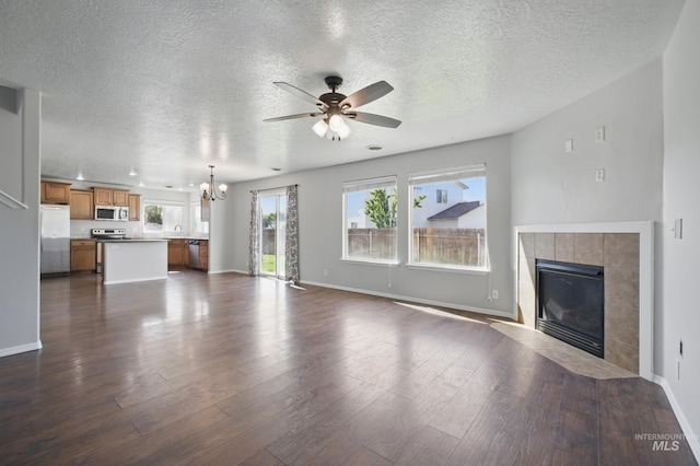 841 Shire St, Middleton, ID 83644 - unfurnished living room with a chandelier, ceiling fan, a tile fireplace, dark wood-style floors, and a textured ceiling