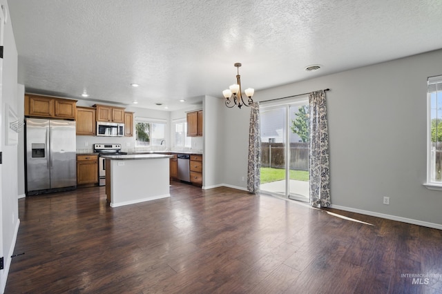 841 Shire St, Middleton, ID 83644 - kitchen featuring appliances with stainless steel finishes, a chandelier, brown cabinetry, dark wood-type flooring, and a kitchen island