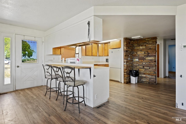 kitchen with dark wood-type flooring, a breakfast bar, white refrigerator, a textured ceiling, and kitchen peninsula