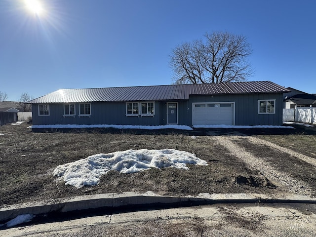 ranch-style house featuring a garage, dirt driveway, fence, and metal roof