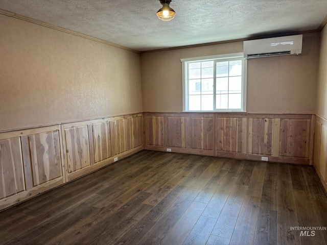 unfurnished room with a textured ceiling, a wainscoted wall, dark wood-type flooring, a wall mounted air conditioner, and crown molding