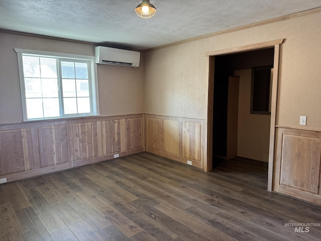 empty room with a wainscoted wall, ornamental molding, dark wood-style flooring, a textured ceiling, and a wall mounted AC