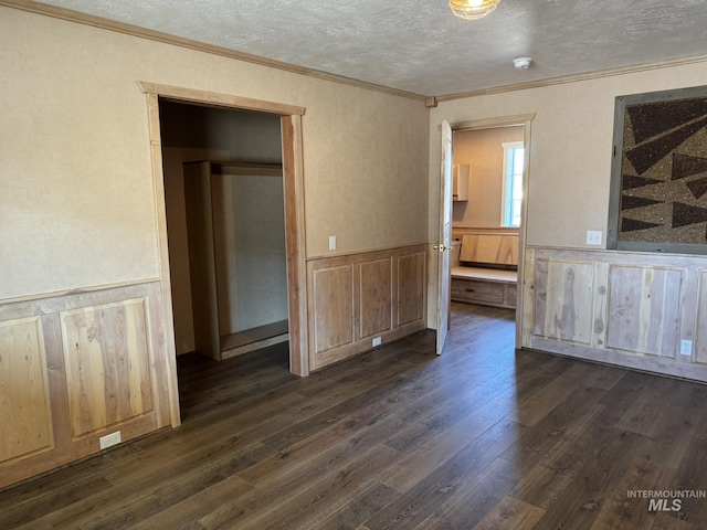 interior space with a wainscoted wall, dark wood-style floors, a textured ceiling, and ornamental molding