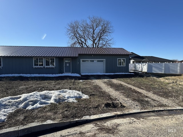 ranch-style home featuring a garage, metal roof, dirt driveway, and fence