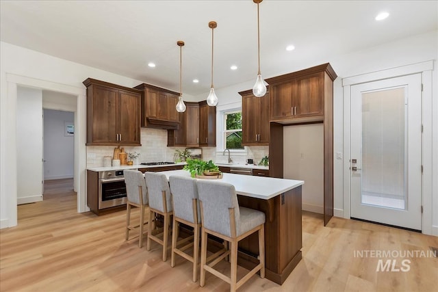 kitchen featuring a center island, sink, hanging light fixtures, light hardwood / wood-style flooring, and stainless steel appliances