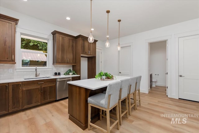 kitchen featuring decorative backsplash, stainless steel dishwasher, sink, pendant lighting, and light hardwood / wood-style flooring