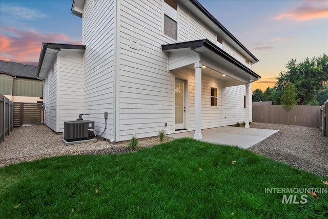 back house at dusk featuring central air condition unit, a patio, and a yard