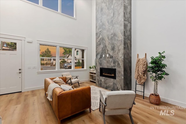 living room with a fireplace, a towering ceiling, a healthy amount of sunlight, and light wood-type flooring