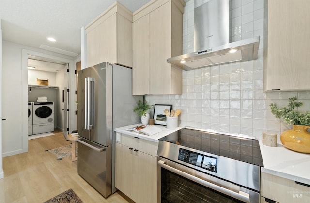4340 E Haystack St Unit 205, Boise, ID 83716 - kitchen featuring wall chimney exhaust hood, stainless steel appliances, washer and dryer, light wood-style flooring, and backsplash