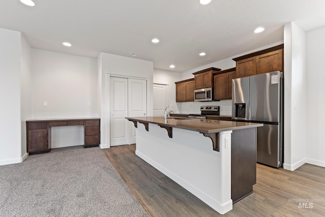 kitchen featuring a kitchen bar, appliances with stainless steel finishes, a kitchen island with sink, and dark wood-type flooring