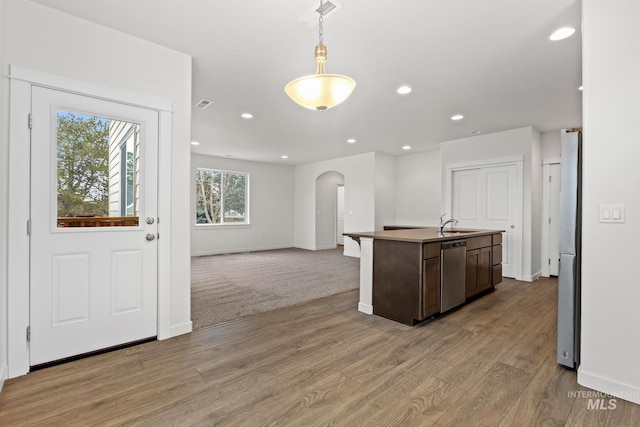 kitchen featuring dark brown cabinetry, pendant lighting, a kitchen island with sink, appliances with stainless steel finishes, and light wood-type flooring