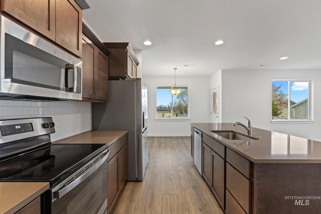 kitchen with appliances with stainless steel finishes, light wood-type flooring, tasteful backsplash, sink, and hanging light fixtures