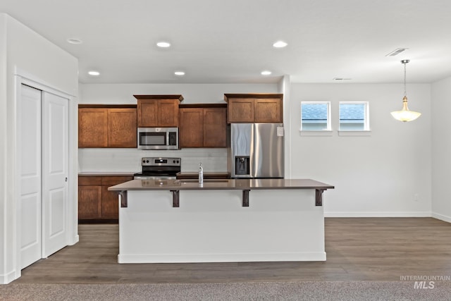 kitchen featuring tasteful backsplash, an island with sink, decorative light fixtures, a kitchen bar, and appliances with stainless steel finishes