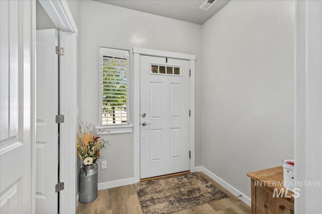 foyer entrance with baseboards, wood finished floors, and visible vents