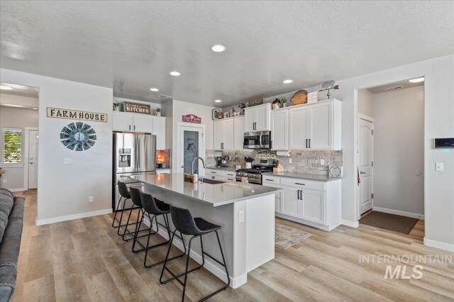kitchen with a breakfast bar area, backsplash, a sink, light wood finished floors, and stainless steel appliances