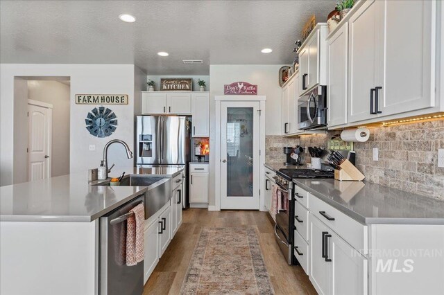 kitchen with a kitchen island with sink, appliances with stainless steel finishes, light wood-type flooring, a sink, and white cabinets