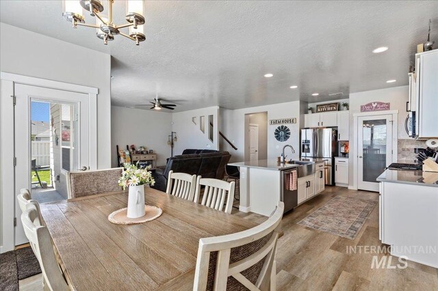 dining space featuring recessed lighting, ceiling fan with notable chandelier, light wood-type flooring, and stairs