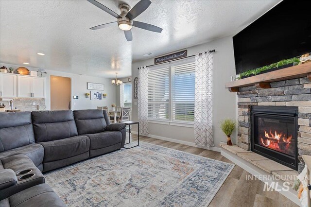 living area with a textured ceiling, light wood-type flooring, ceiling fan with notable chandelier, and a fireplace