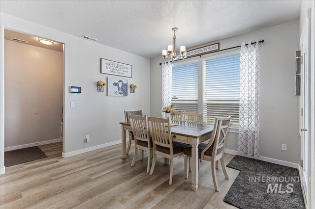 dining area with an inviting chandelier, a textured ceiling, light wood-style floors, and baseboards