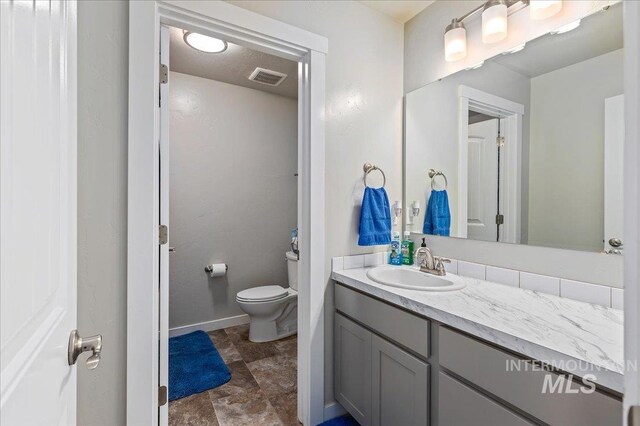 bathroom with stone finish flooring, visible vents, vanity, baseboards, and toilet