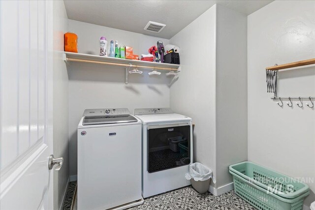 clothes washing area with baseboards, visible vents, laundry area, and washing machine and clothes dryer